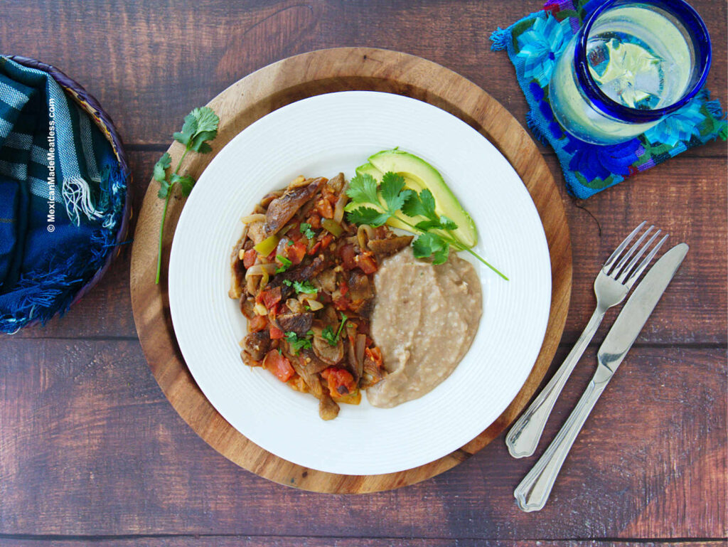 Bistec a la mexicana or Mexican style steak served with refried beans and avocado slices.