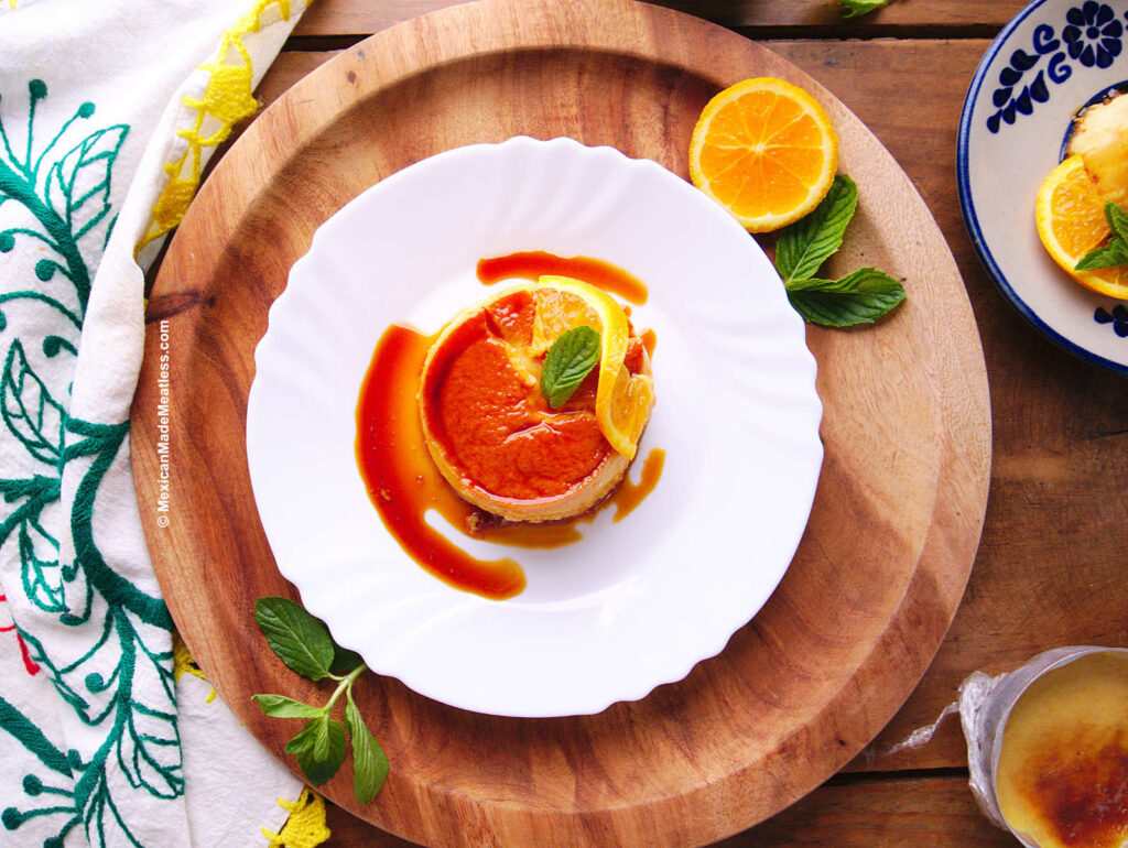 Individual La Lechera flan served with a slice of orange on a white plate.