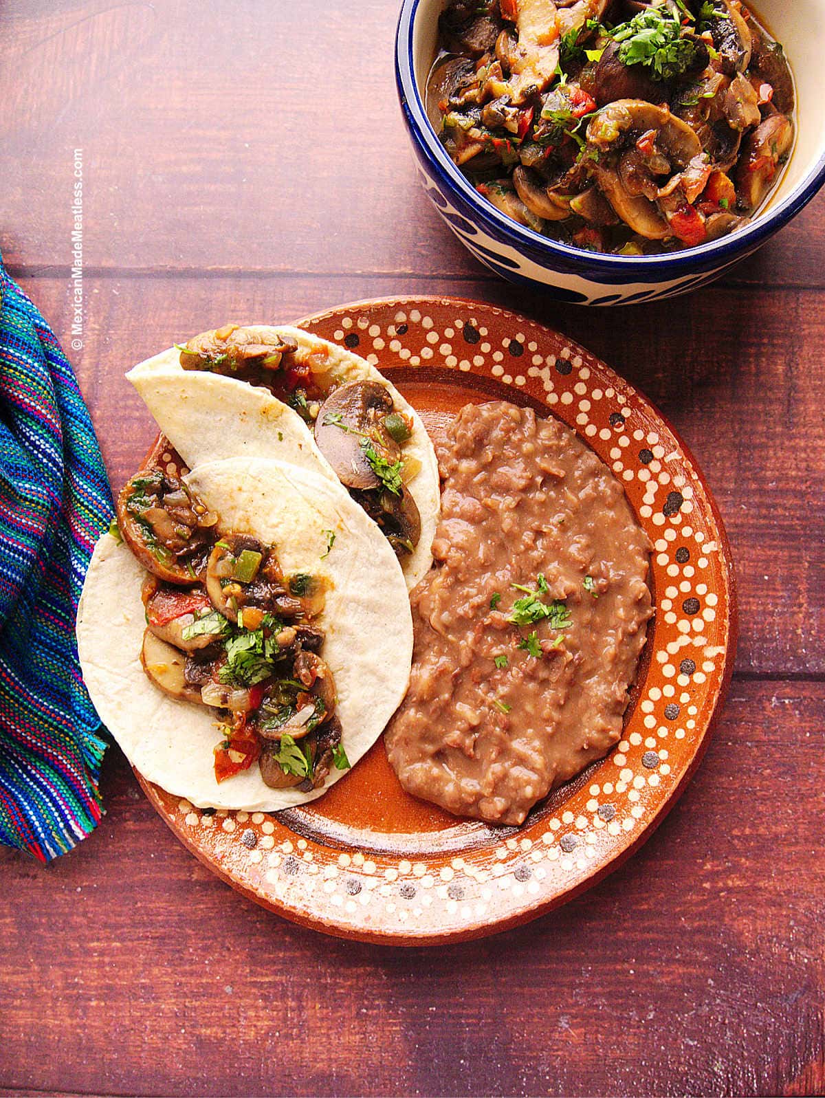 Mushroom tacos with a side of refried beans on a decorative Mexican terracotta plate.