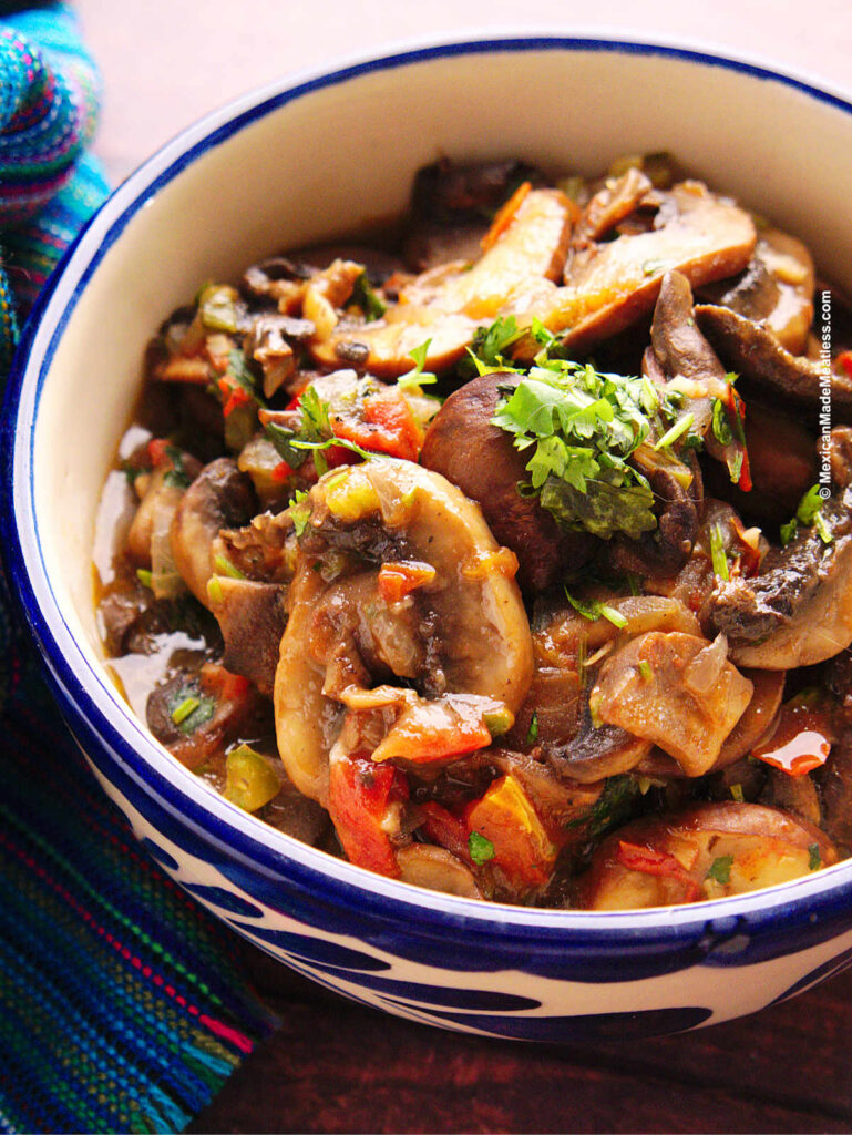 Button mushrooms cooked Mexican-style with onion, tomato and jalapeno, inside a small bowl. 