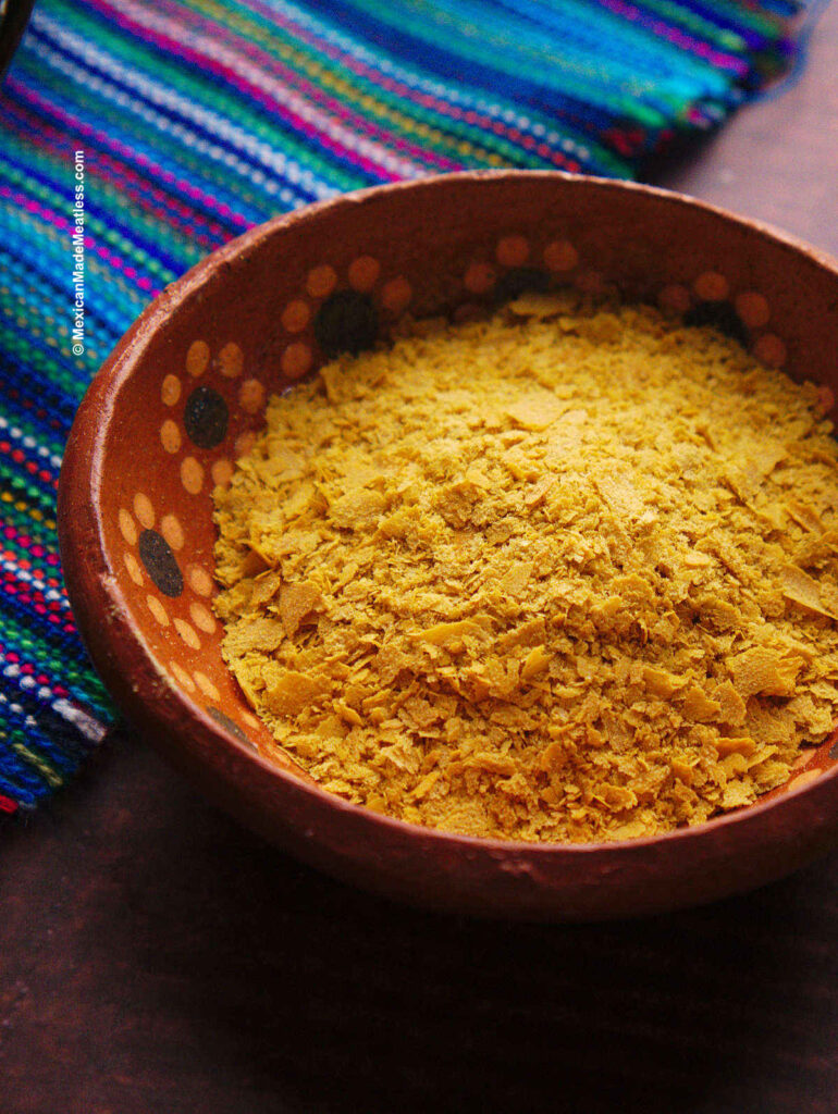 Nutritional yeast flakes inside a small brown bowl.
