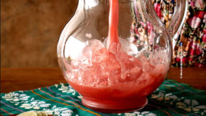 Pouring Mexican watermelon juice into a pitcher filled with ice cubes.