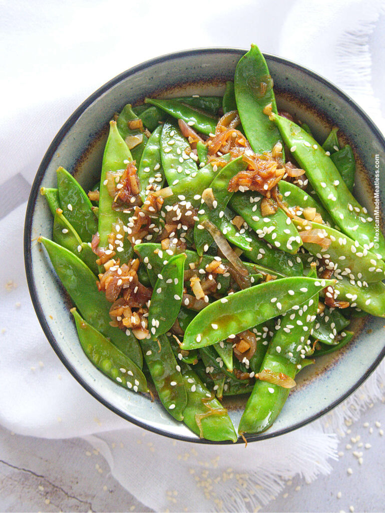 Sautéed snow peas cooked with shallots, garlic, ginger and sriracha sauce, served inside a small grey bowl. 