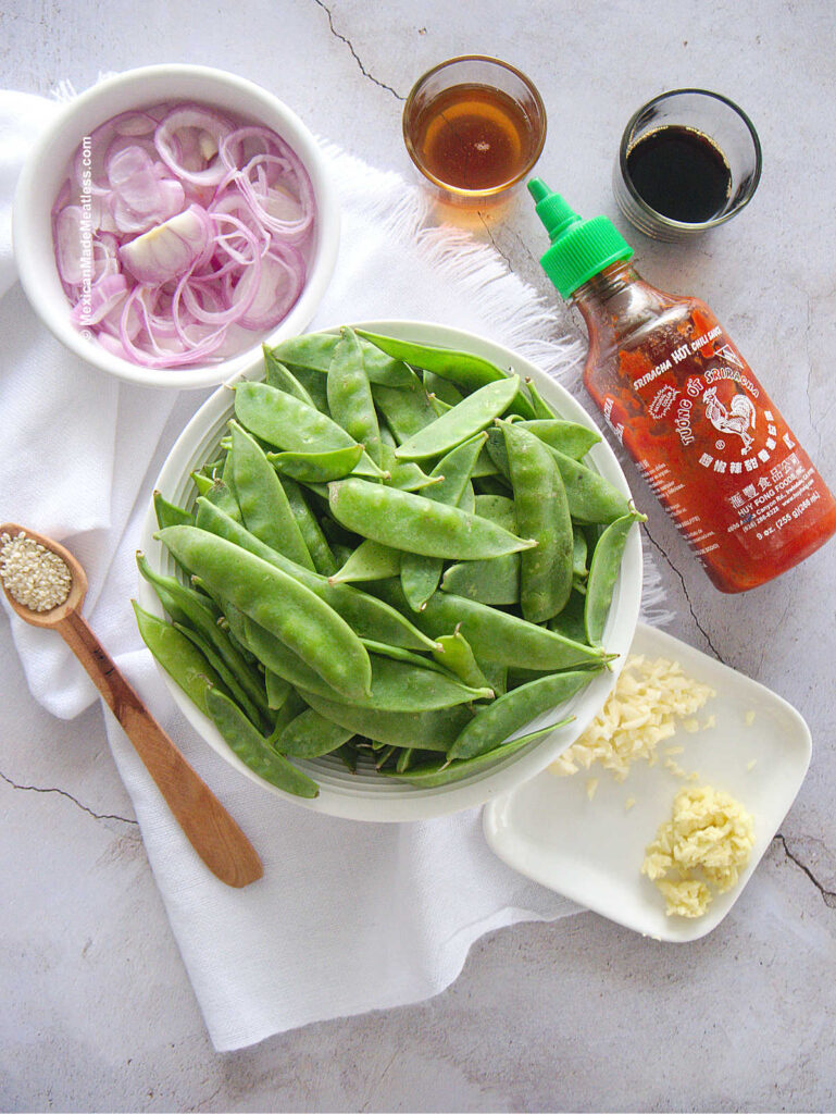 Fresh snow peas, shallots, garlic, ginger, sriracha and sesame seeds and oil in small bowls.