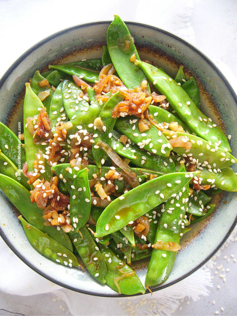 Small bowl filled with sauteed snow peas with sesame seeds.