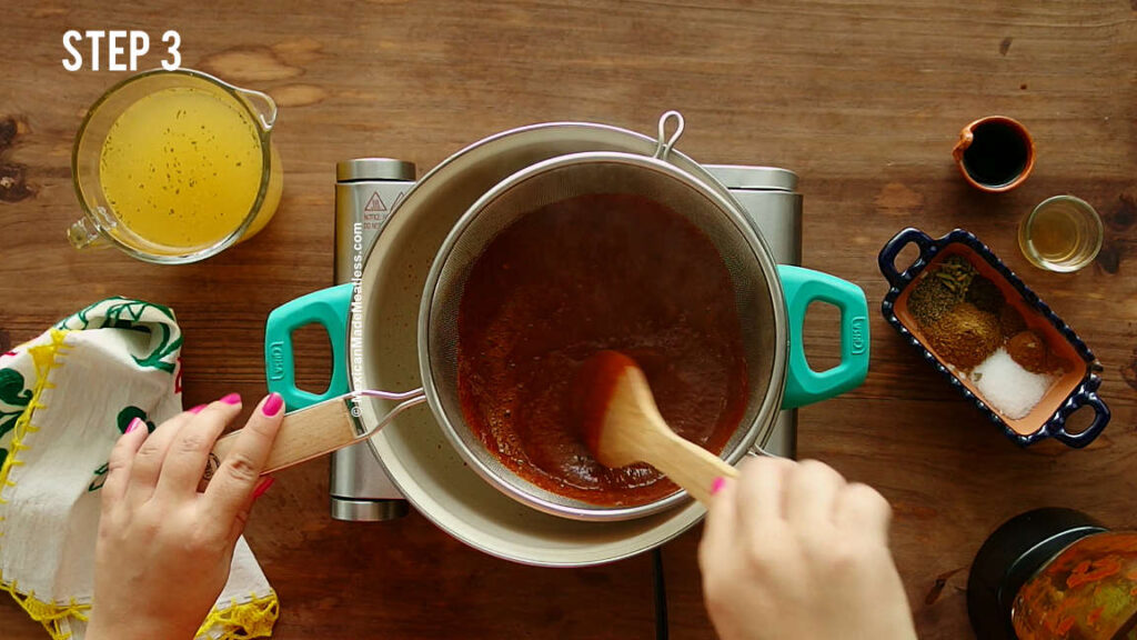 Straining red chile sauce into a pot to make vegan birria tacos.