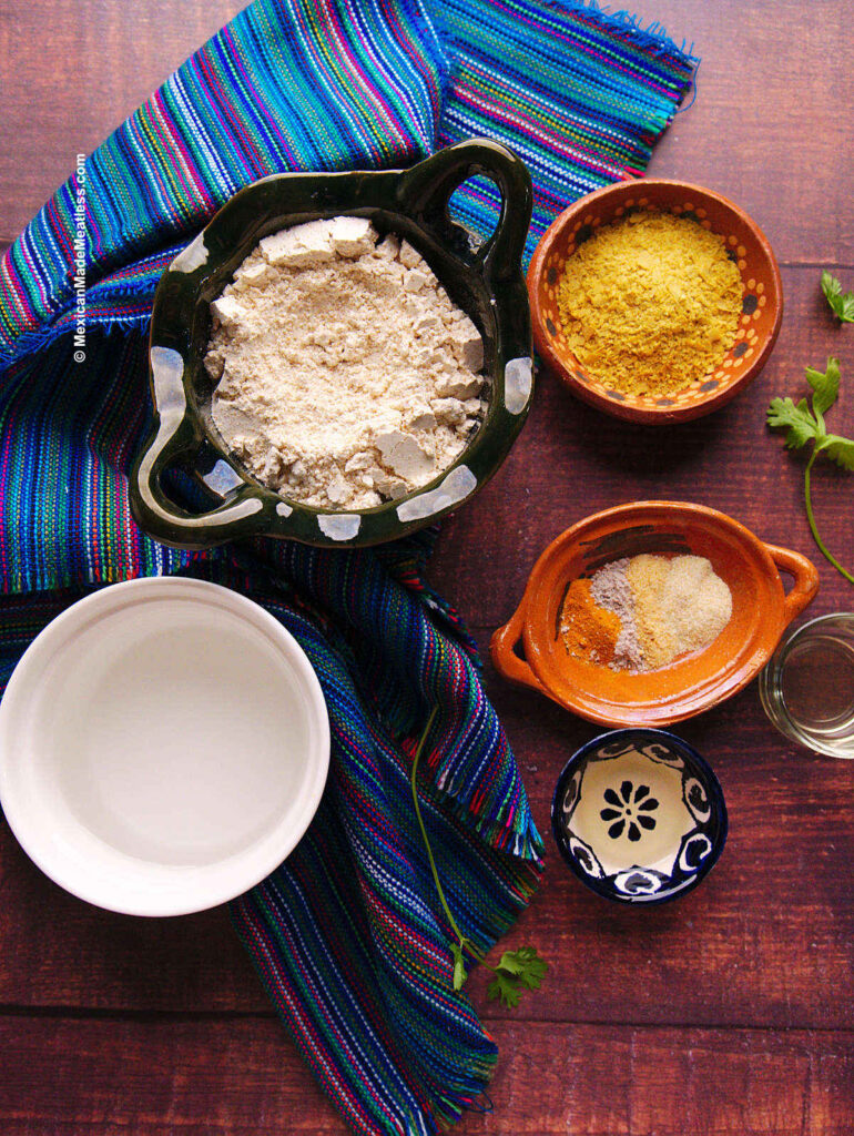 Ingredients in small bowls that are used in making a vegan omelette with chickpea flour. There is chickpea flour, nutritional yeast, turmeric, spices, oil, vinegar and water.