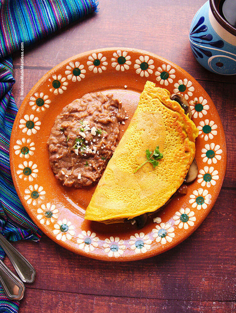 A vegan omelette filled with sautéed mushrooms and some refried beans on the side.