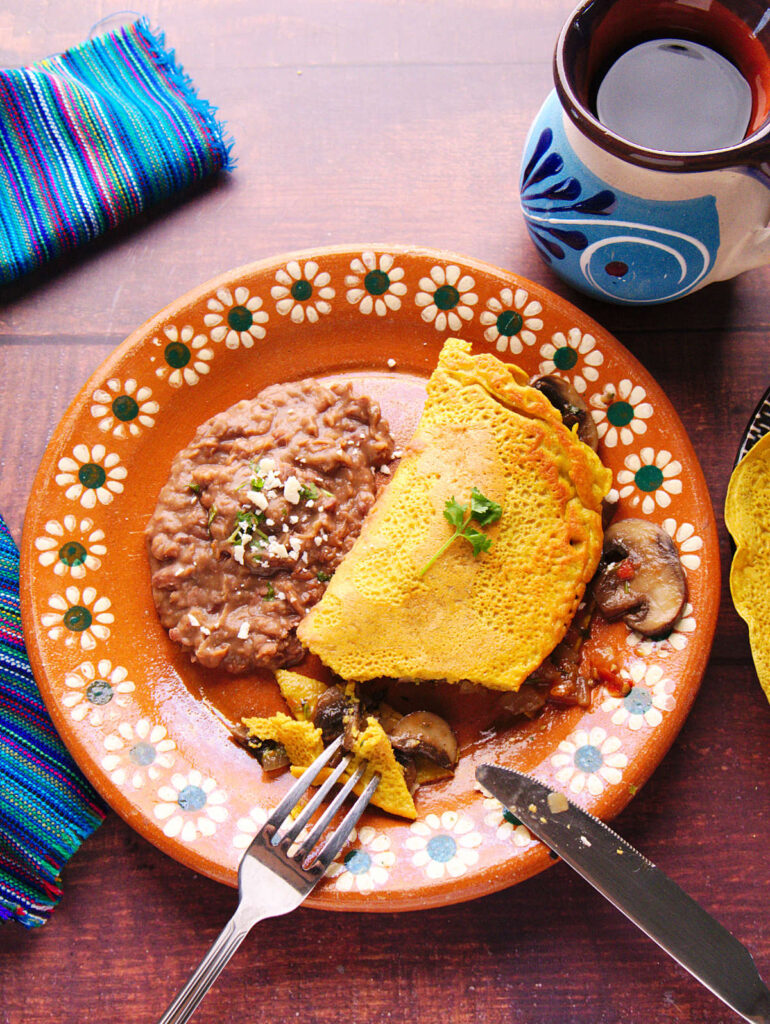 Vegan omelette filled with mushrooms and a side of refried beans and a black coffee. 