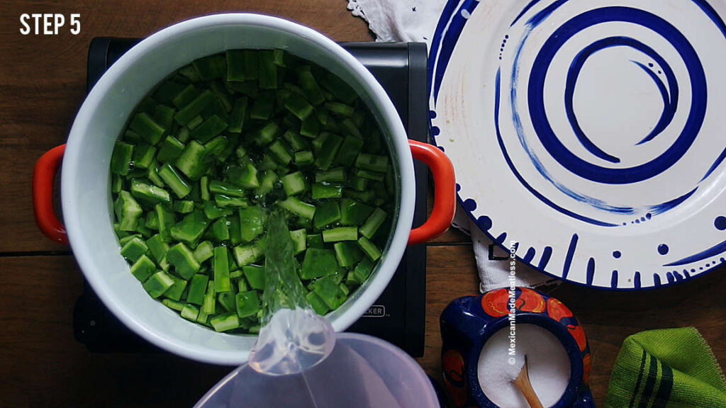 Pouring water over chopped nopales inside a pot to boil them. 