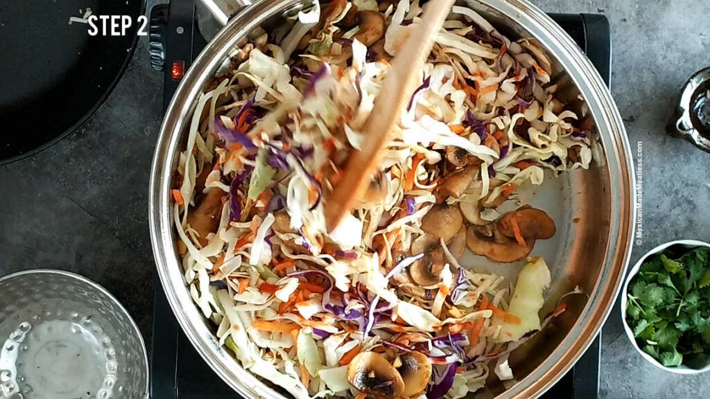 Mixing in coleslaw mix into the pan for cooking vegan egg roll bowls. 
