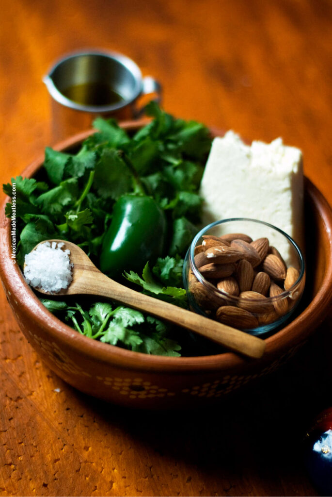 A bowl full of ingredients for Mexican cilantro pesto: fresh cilantro, cotija cheese, almonds, garlic, salt and olive oil.