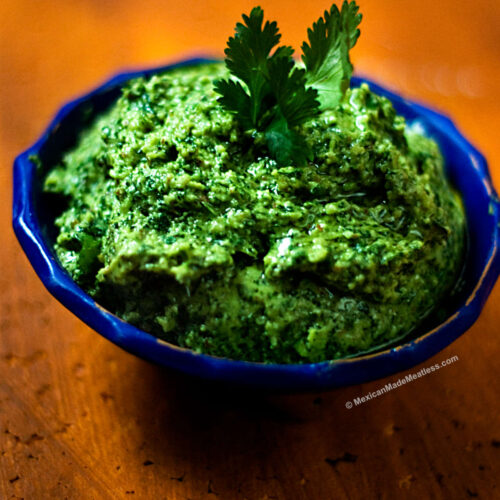 Cilantro pesto with a Mexican twist inside a small blue bowl and on a burnt orange table.