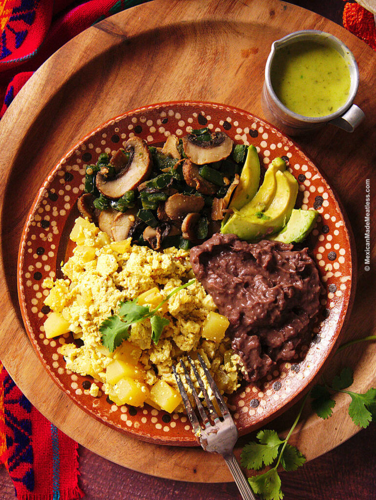 A plate full of Mexican potatoes and eggs, avocado slices and refried black beans. 