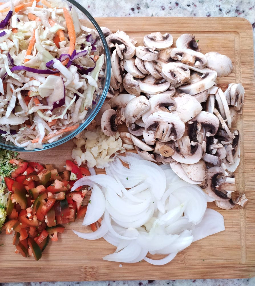 Ingredients for making vegan egg roll bowl: coleslaw mix, mushrooms, onion, garlic and chopped red chili. 