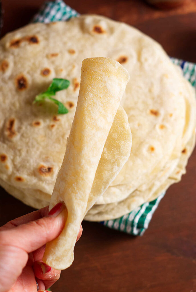 A woman's hand holding a rolled up flour tortilla.