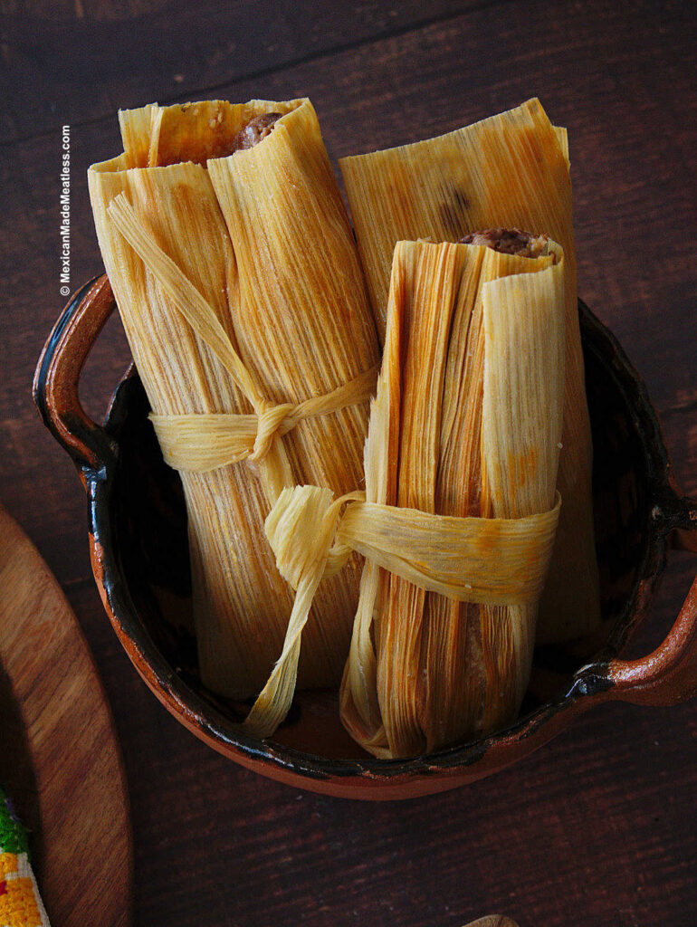 Three bean and cheese tamales standing upright inside a small bowl. 
