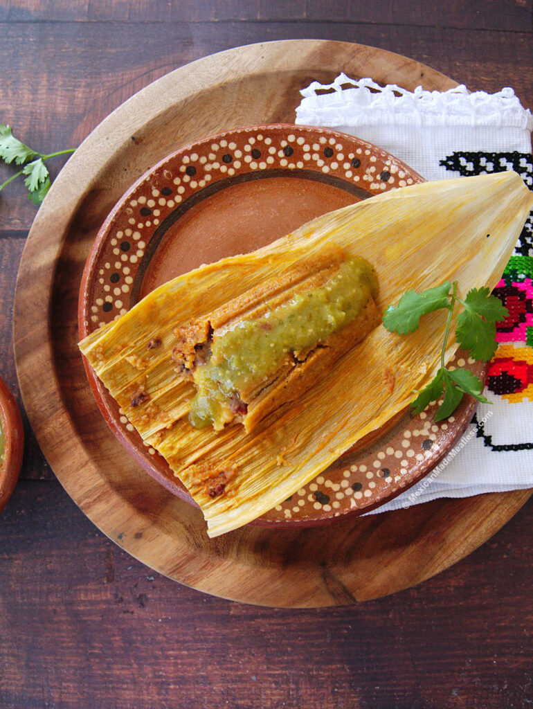Once bean and cheese tamale on top of a corn husk and drizzled with salsa verde.