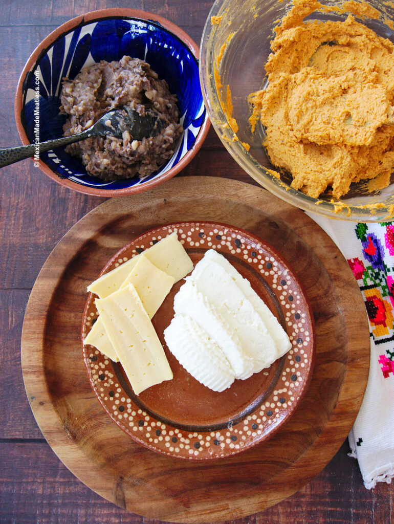 A brown table with refried beans, tamales masa dough, and slices of cheese.