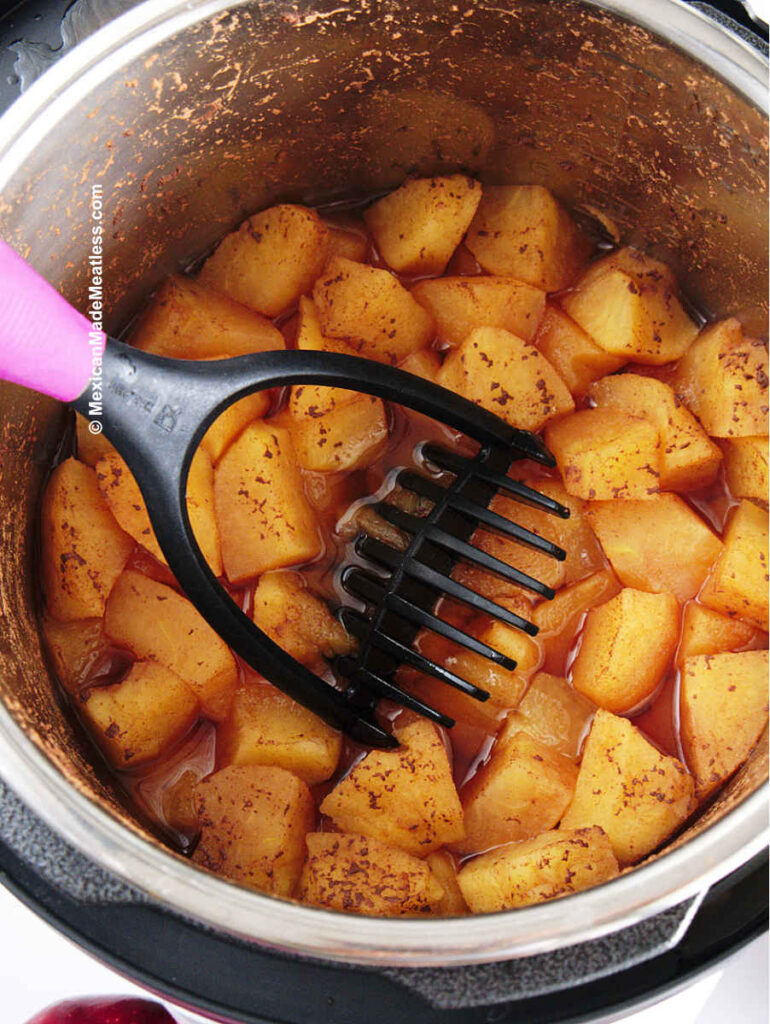 Mashing cooked apples with a potato masher to make apple puree. 