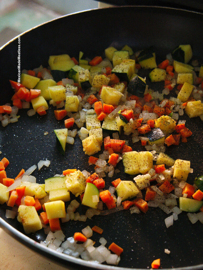 Sautéing carrot, onion, garlic and zucchini in a black pan. 