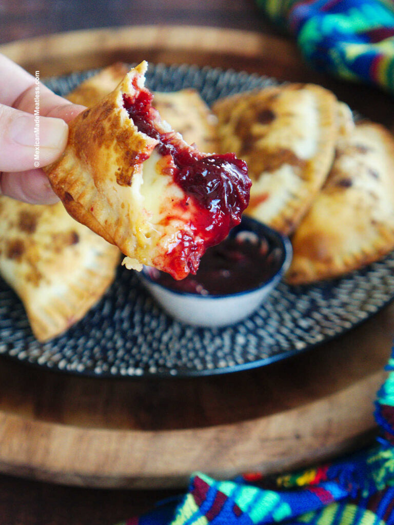 Close up view of a crispy empanada turnover filled with cranberry sauce and cheese.