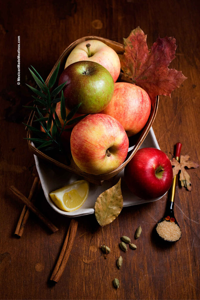 Different types of apples inside a small wooden basket on a brown table.