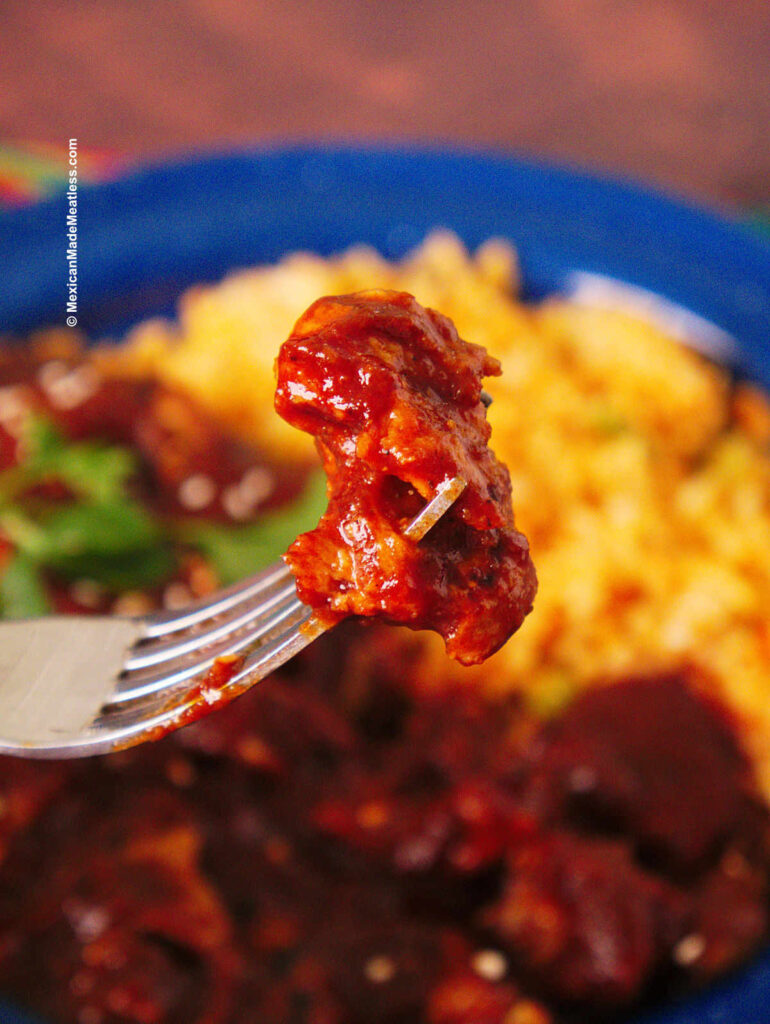 Close up view of seitan cooked in red mole sauce and served with Mexican red rice.