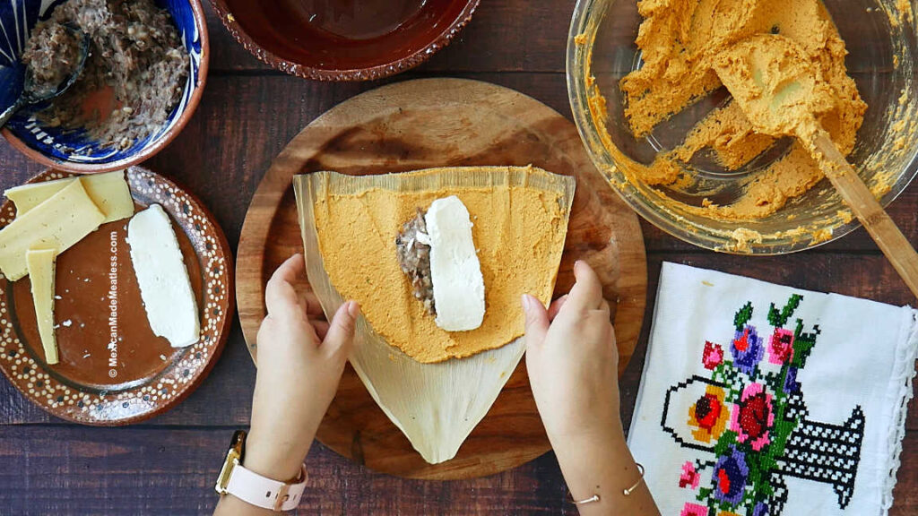 Assembling bean and cheese tamales on a brown table. 