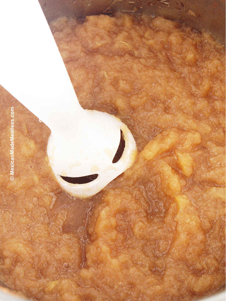An immersion blender pureeing cooked apples to make vegan applesauce.