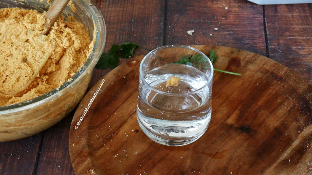 A small drop or red tamale masa dough floating in a glass of water to check that the masa is ready.
