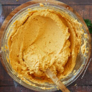 A big glass mixing bowl filled with red masa for tamales.