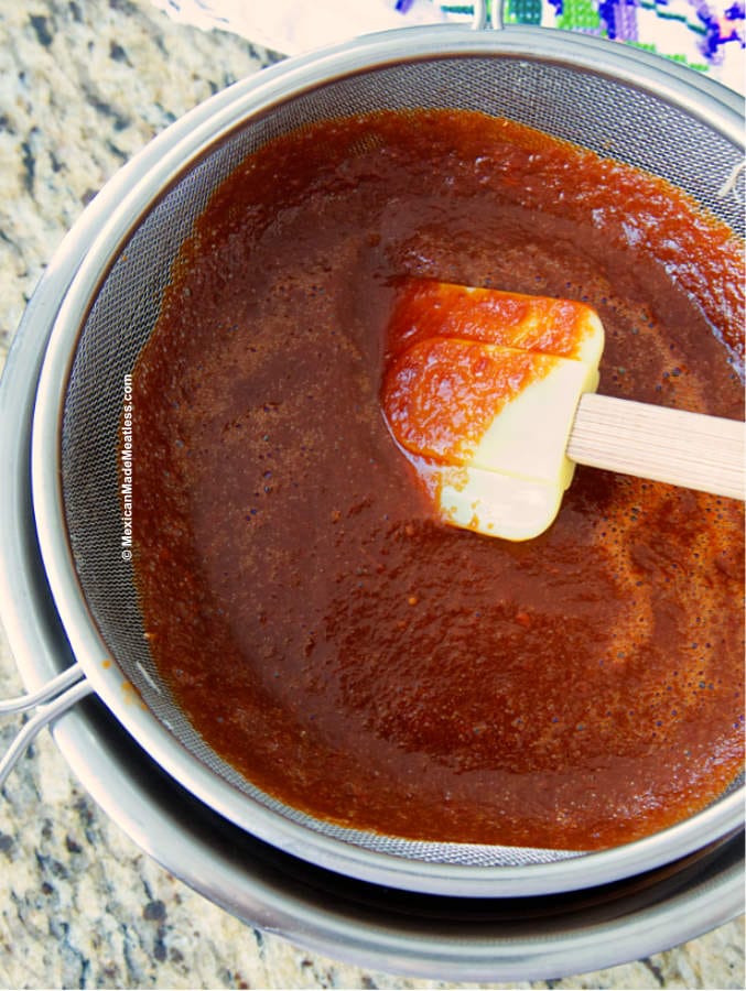 Straining red chili sauce into a bowl to make tamales.