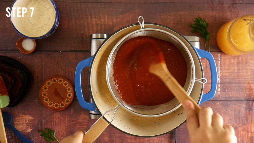 Straining mole salsa through a fine sieve and into a blue pot.