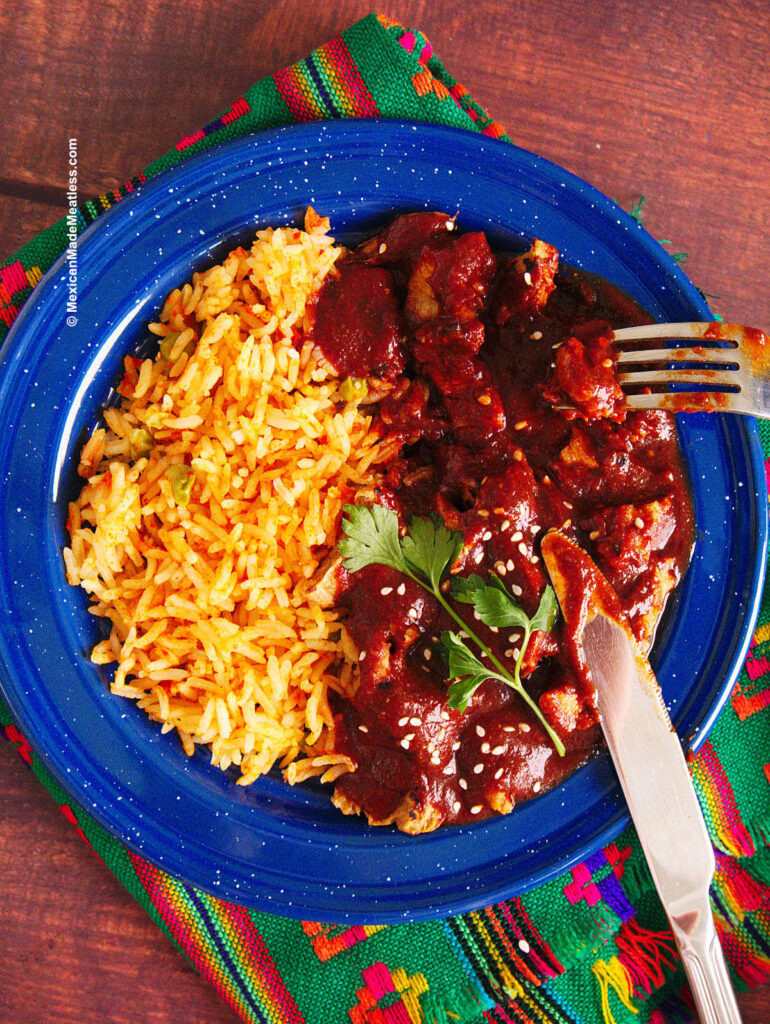A blue plate filled with Mexican rice and red mole ranchero.