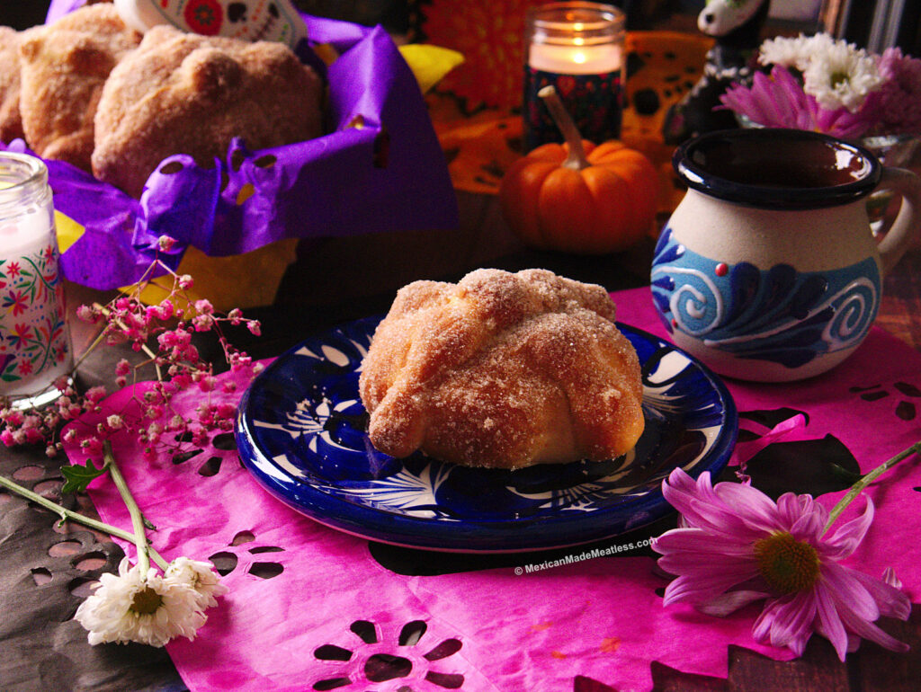 One small Mexican pan de muerto on a blue and white plate with a cup of hot chocolate on the side. 