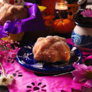 One small Mexican pan de muerto on a blue and white plate with a cup of hot chocolate on the side.