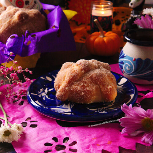 One small Mexican pan de muerto on a blue and white plate with a cup of hot chocolate on the side.