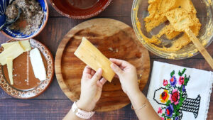 A woman's hand holding a rolled up vegetarian bean and cheese tamale.