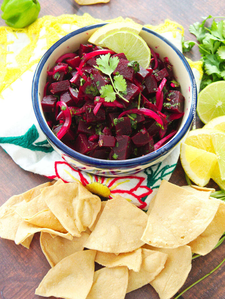 Yucatan style beet salad served inside a small blue and white bowl and tortilla chips all around.