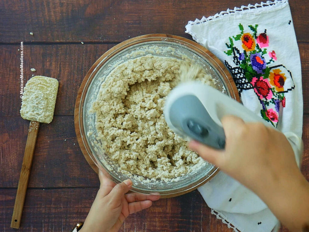 Mixing defrosted tamale dough in a large glass mixing bowl with a handheld mixer. 