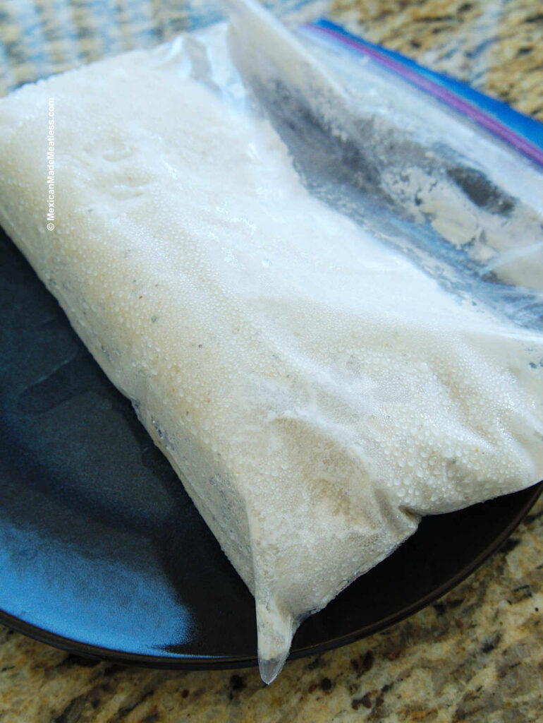 A Ziploc bag filled with frozen masa for tamales defrosting on a kitchen counter. 