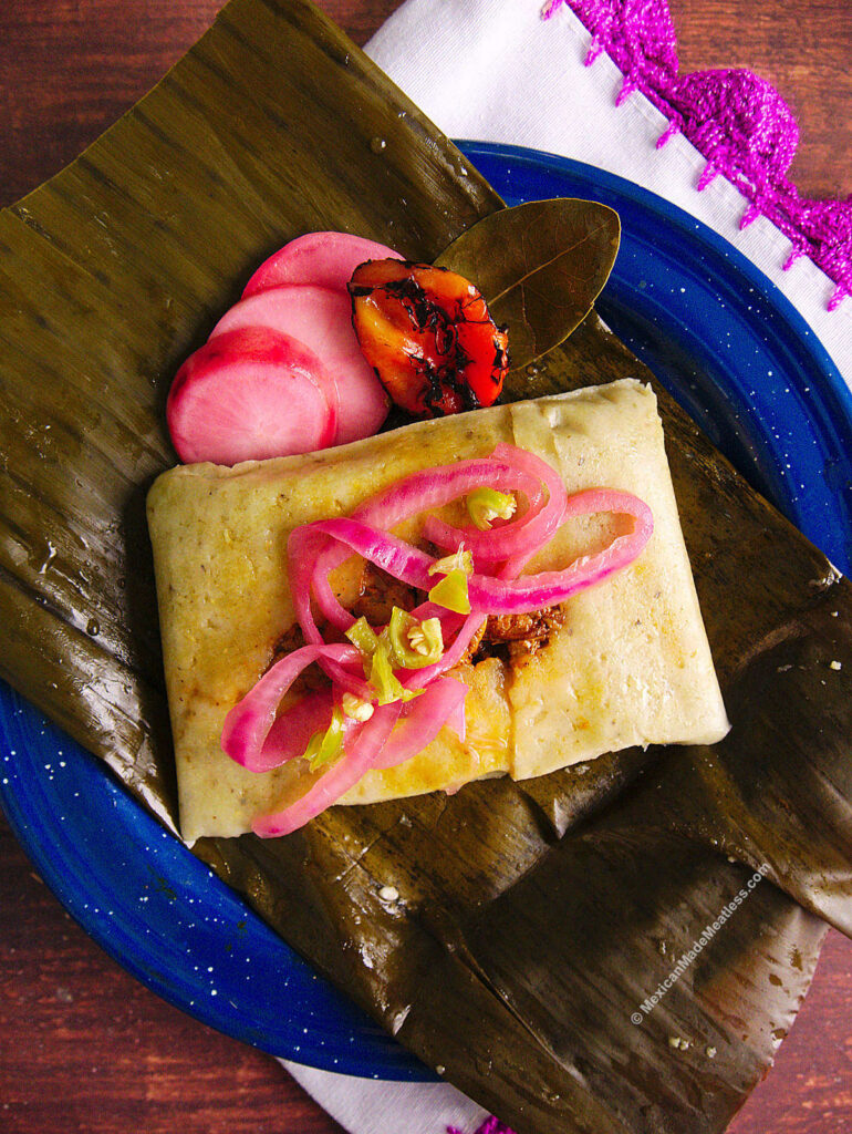 One banana leaf tamale topped with pickled red onion and a habanero pepper.