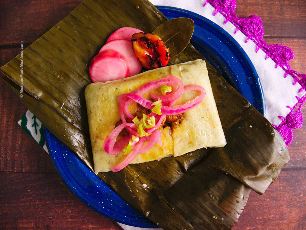 One banana leaf tamale topped with pickled red onion and a habanero pepper.