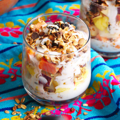 A cup filled with Mexican bionicos fruit salad with sweet cream sauce, granola, nuts and coconut flakes.