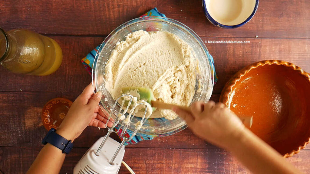 Making tamale dough in a large glass mixing bowl with a hand mixer.