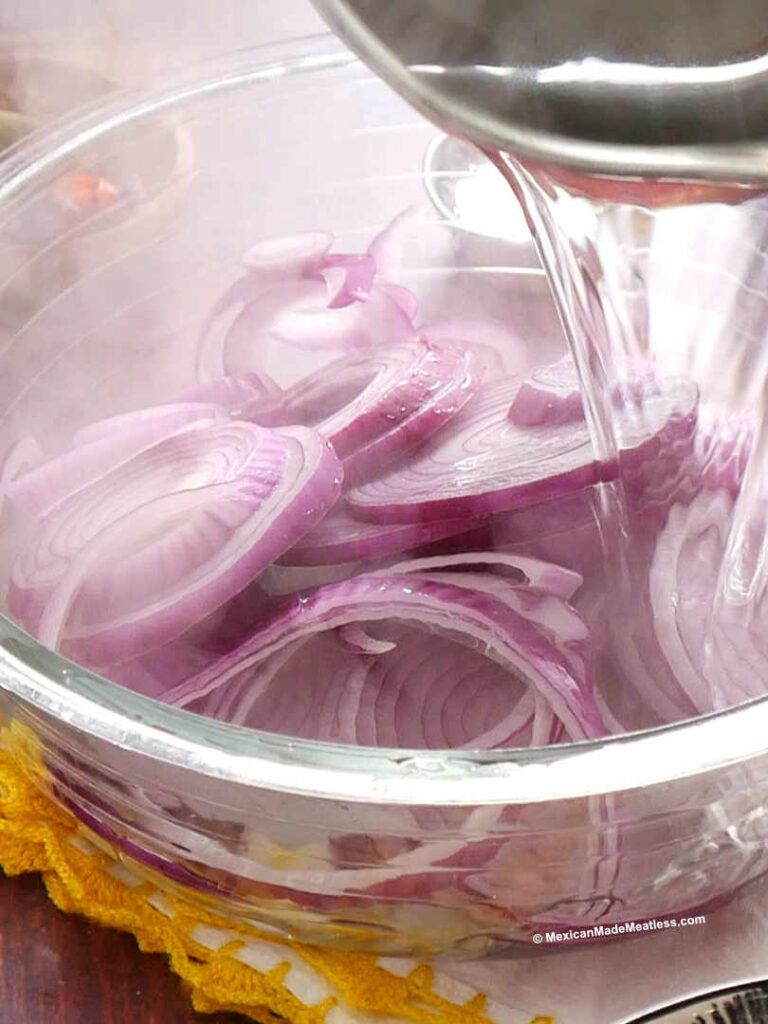 Adding hot boiling water over sliced red onions before pickling them. 