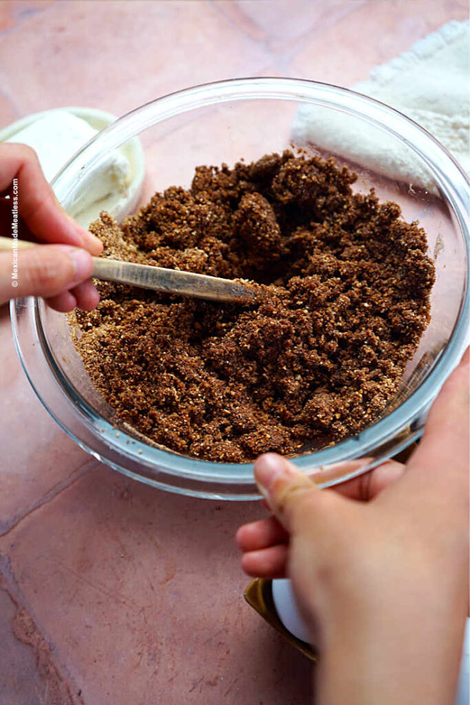 Mixing cookie crumbs with chopped pecans, cacao powder, cinnamon and melted butter in a small glass bowl.