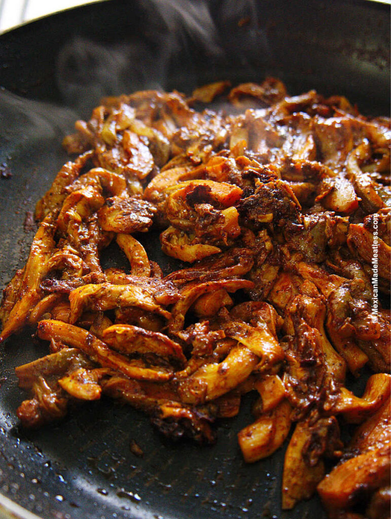 A large frying pan cooking oyster mushrooms in cochinita pibil sauce.