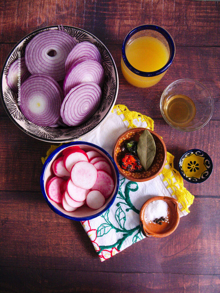 Small bowls filled with the ingredients for making Mexican pickled onions. They are red onions, radishes, habanero peppers, bay leaf, salt, peppercorns, apple cider vinegar, orange juice, olive oil. 